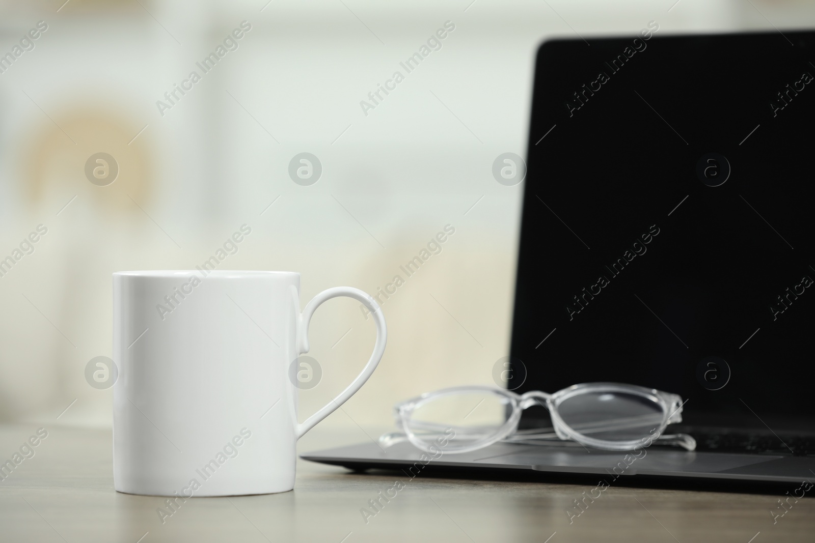 Photo of White ceramic mug, glasses and laptop on wooden table indoors. Space for text