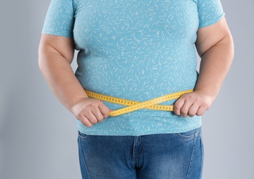 Overweight woman measuring waist before weight loss on color background