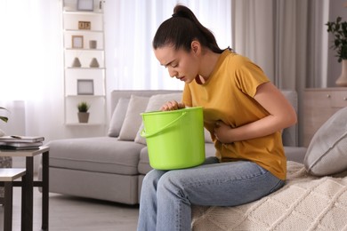 Photo of Young woman with bucket suffering from nausea at home, space for text. Food poisoning