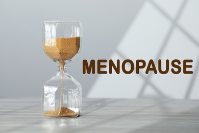 Image of Menopause word and hourglass on table against light background