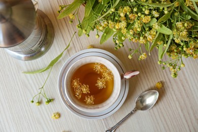 Photo of Cup of aromatic tea with linden blossoms on white wooden table, flat lay