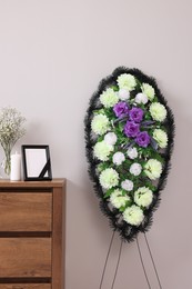 Photo of Wreath of plastic flowers and frame with black ribbon, burning candle on commode in room. Funeral attributes