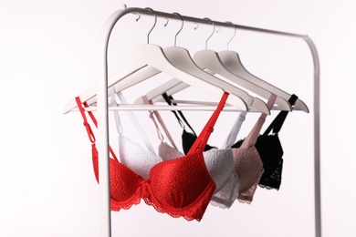 Hangers with beautiful lace bras on rack against white background. Stylish underwear