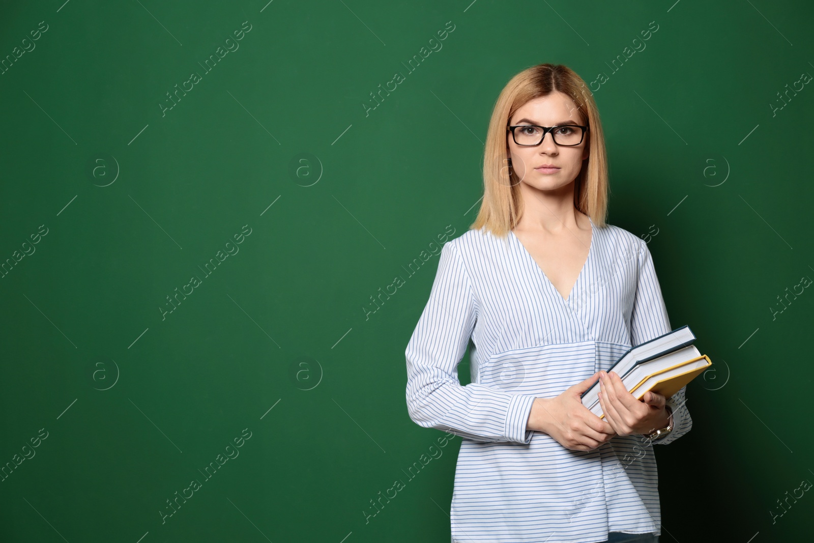 Photo of Portrait of beautiful teacher with books near chalkboard, space for text