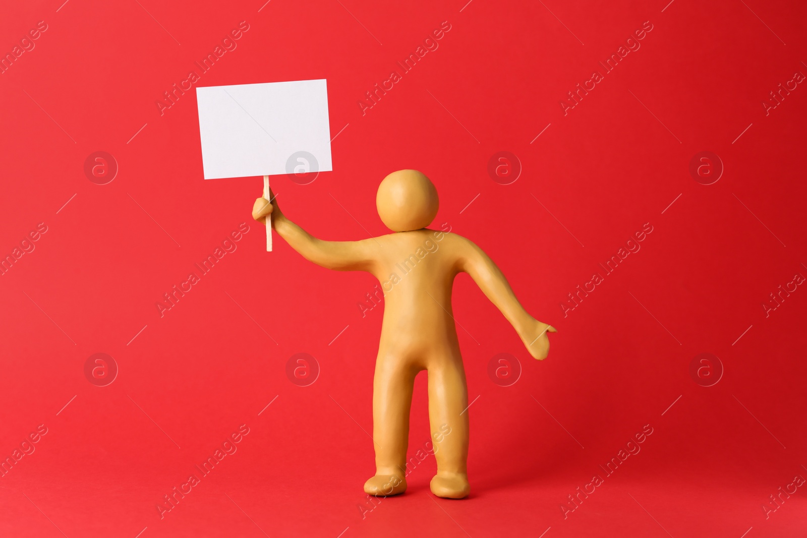 Photo of Human figure made of yellow plasticine holding blank sign on red background