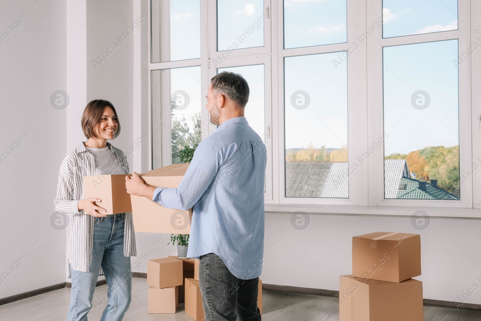 Photo of Happy couple with moving boxes near big window in new apartment