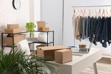 Photo of Store interior with clothing rack, cardboard boxes and laptop. Online selling