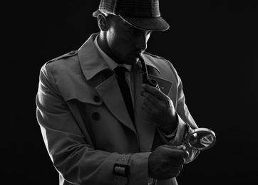 Photo of Old fashioned detective with magnifying glass smoking pipe on dark background, black and white effect