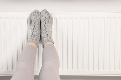Photo of Woman warming feet near heating radiator, closeup. Space for text