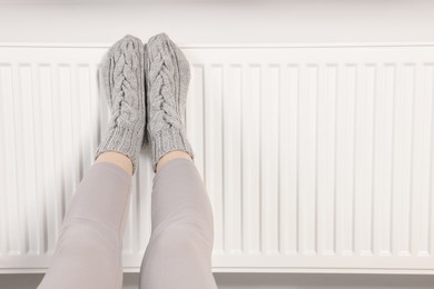 Woman warming feet near heating radiator, closeup. Space for text