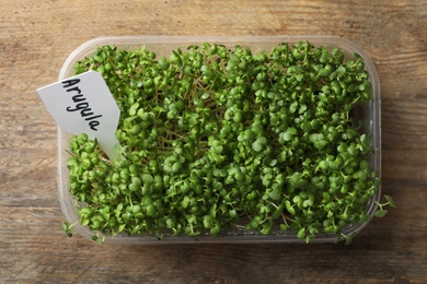 Photo of Sprouted arugula seeds in plastic container on wooden table, top view