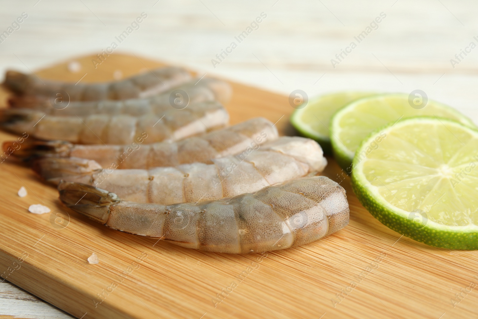 Photo of Fresh raw shrimps and lime on wooden board, closeup