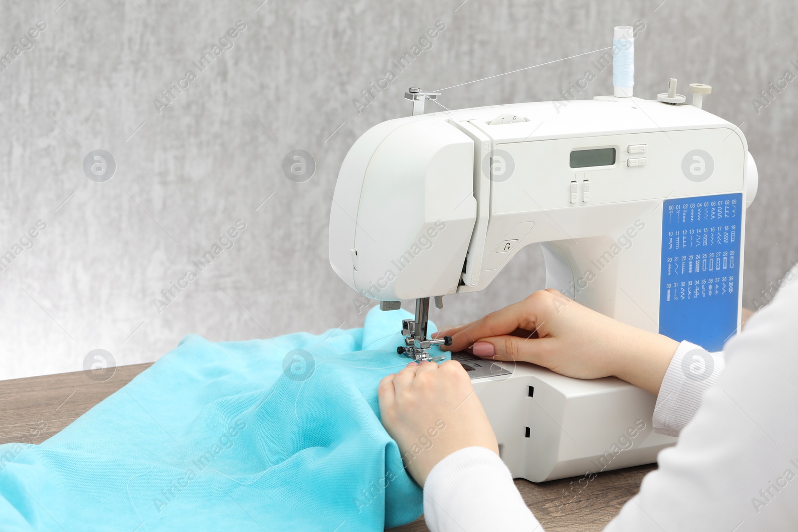 Photo of Seamstress working with sewing machine at table indoors, closeup