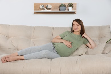 Photo of Happy pregnant woman lying on beige sofa indoors