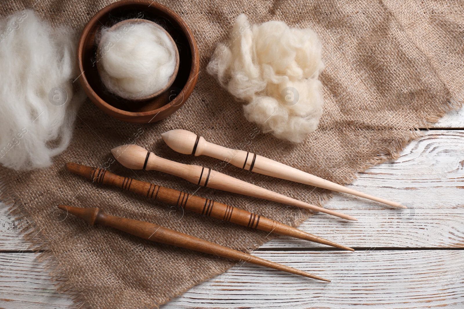 Photo of Soft wool and spindles on white wooden table, flat lay