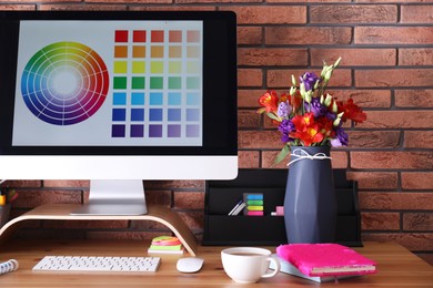 Stylish vase with fresh flowers and computer on wooden table at workplace