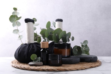Photo of Spa composition with cosmetic products, herbal massage bags, stones and eucalyptus branches on white marble table