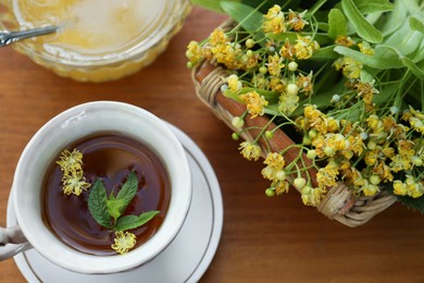 Photo of Cup of hot aromatic herbal tea, honey and linden blossoms on wooden table, above view