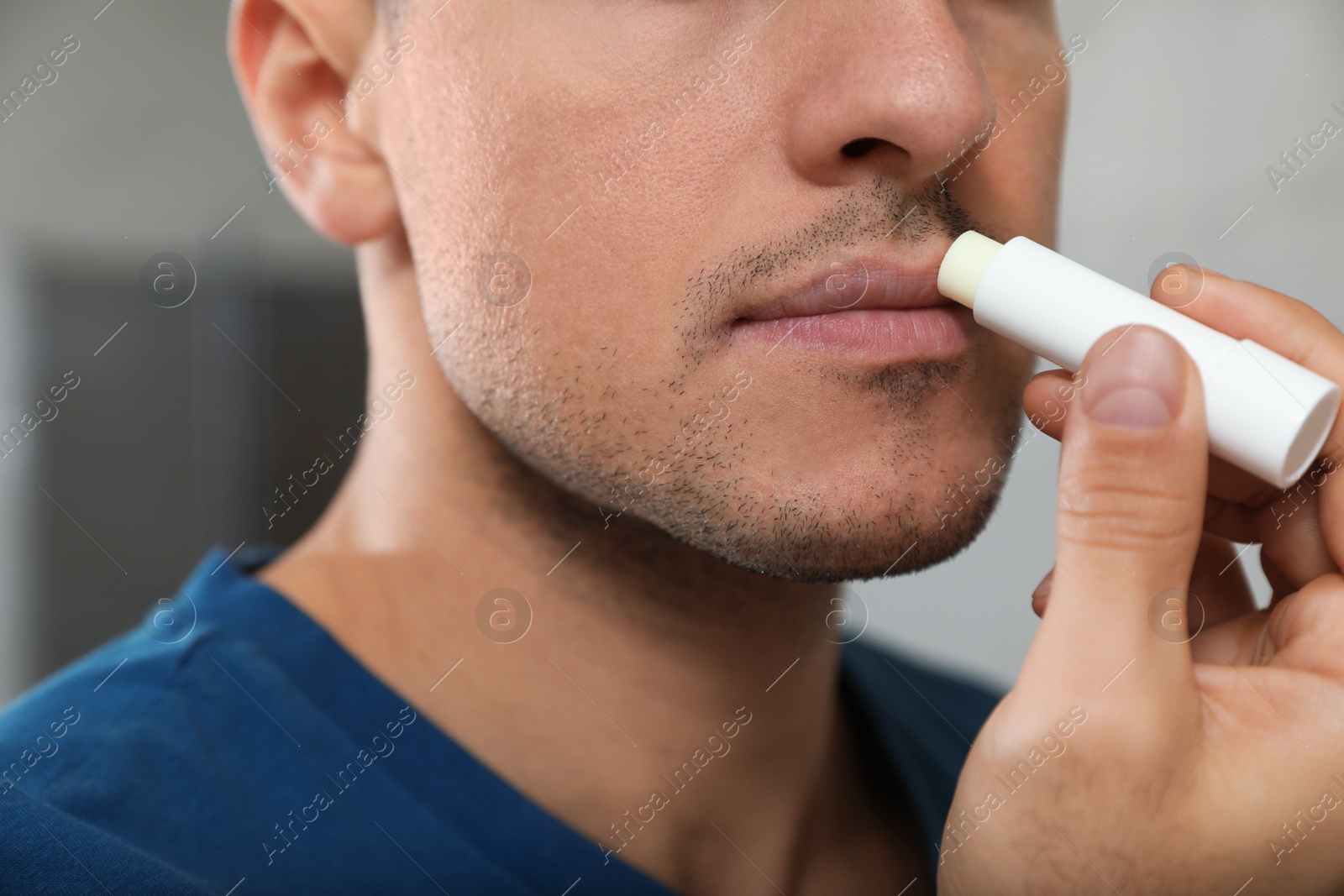 Photo of Man applying hygienic lip balm indoors, closeup