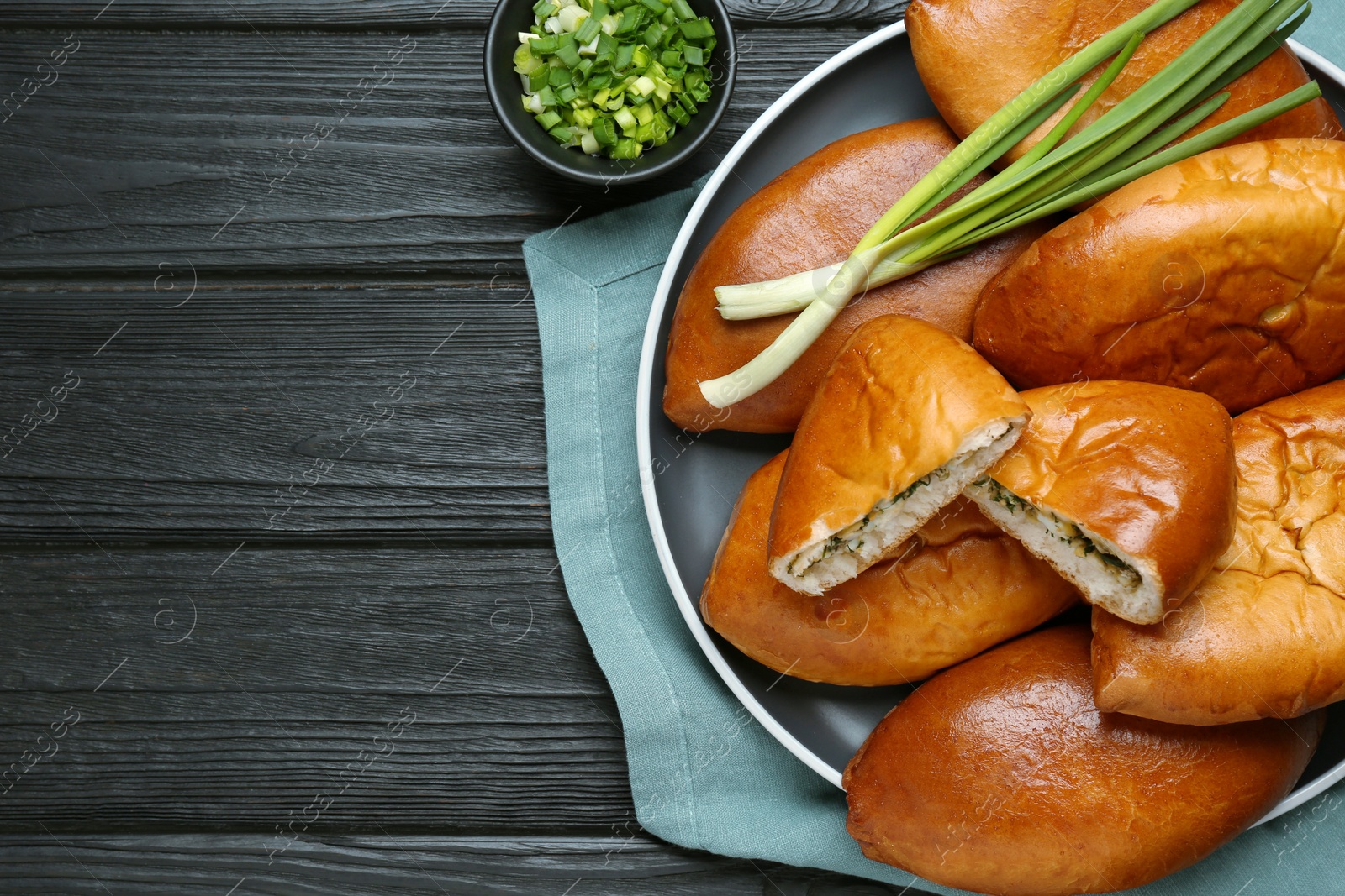 Photo of Many delicious baked patties on black wooden table, flat lay. Space for text