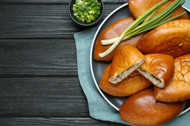 Many delicious baked patties on black wooden table, flat lay. Space for text