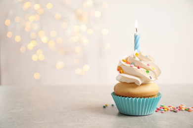 Photo of Birthday cupcake with candle on light grey table against blurred lights. Space for text