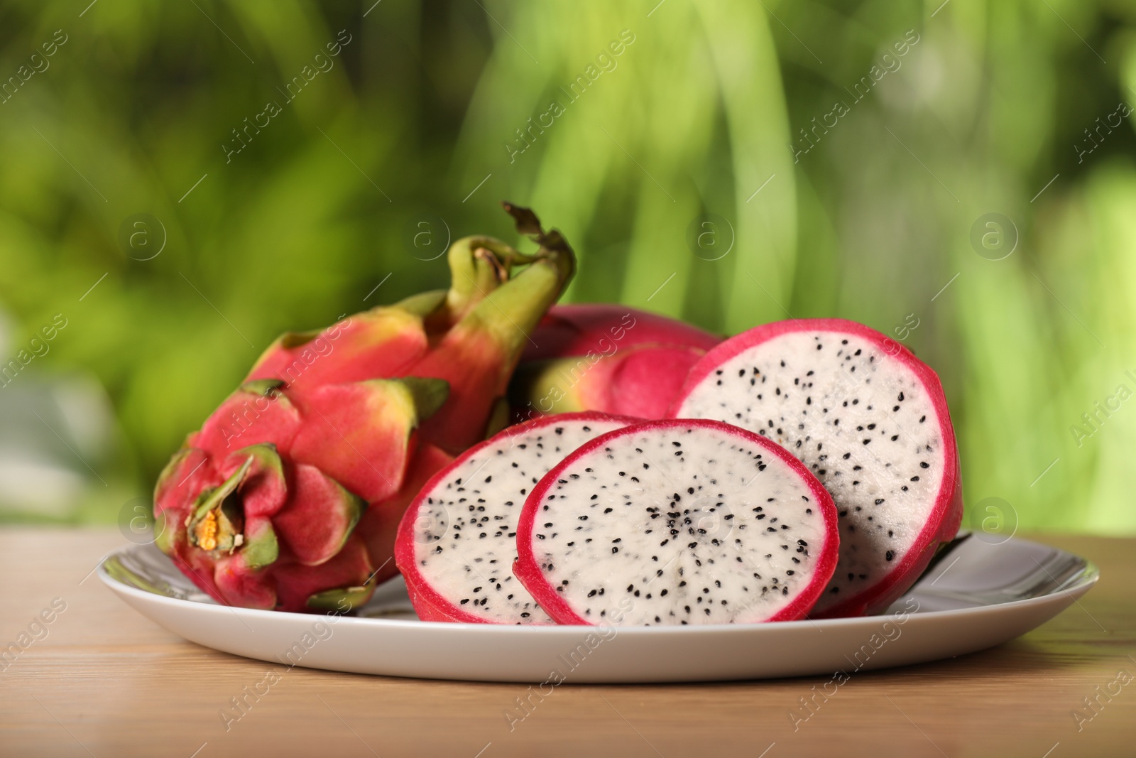 Photo of Tray with delicious cut and whole dragon fruits (pitahaya) on wooden table.