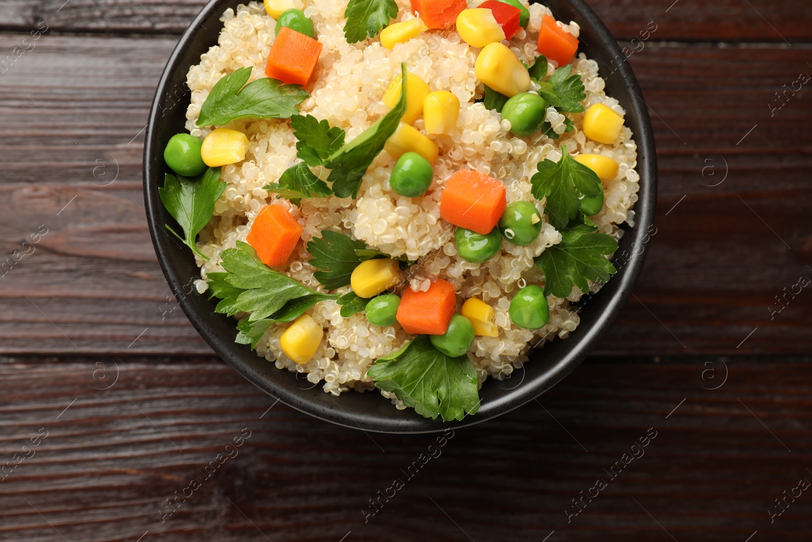 Photo of Tasty quinoa porridge with vegetables in bowl on wooden table, top view