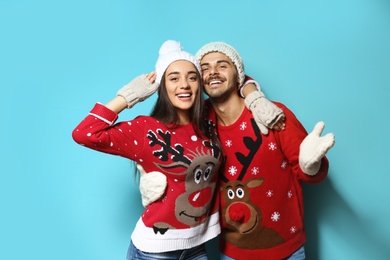 Young couple in Christmas sweaters and knitted hats on color background