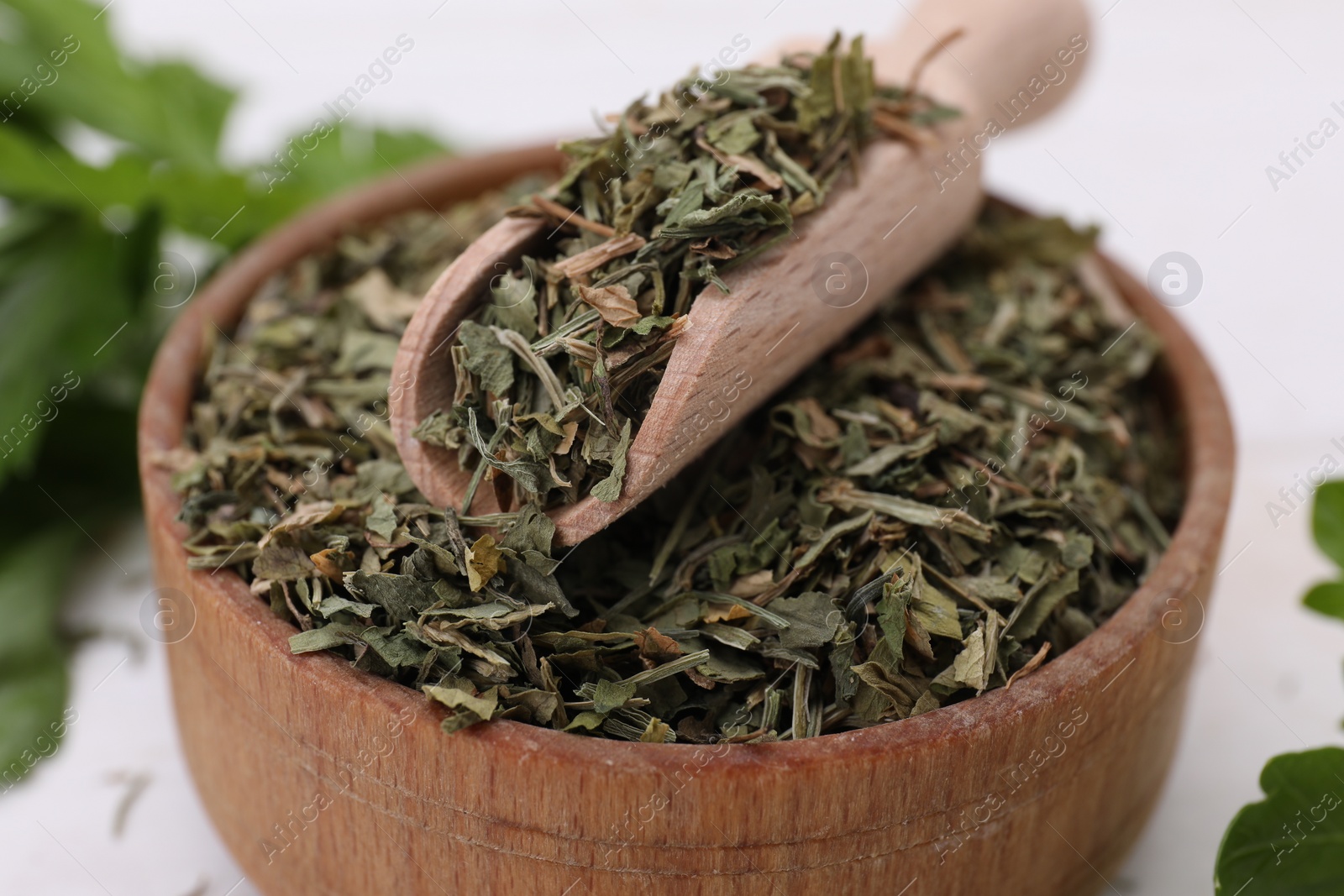 Photo of Dried aromatic parsley and scoop in bowl on white table, closeup