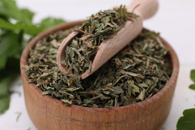 Dried aromatic parsley and scoop in bowl on white table, closeup