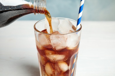 Pouring refreshing soda drink into glass with ice cubes on blurred background, closeup