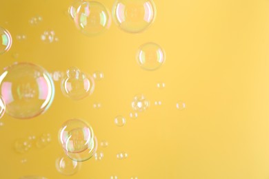 Beautiful transparent soap bubbles on yellow background, space for text