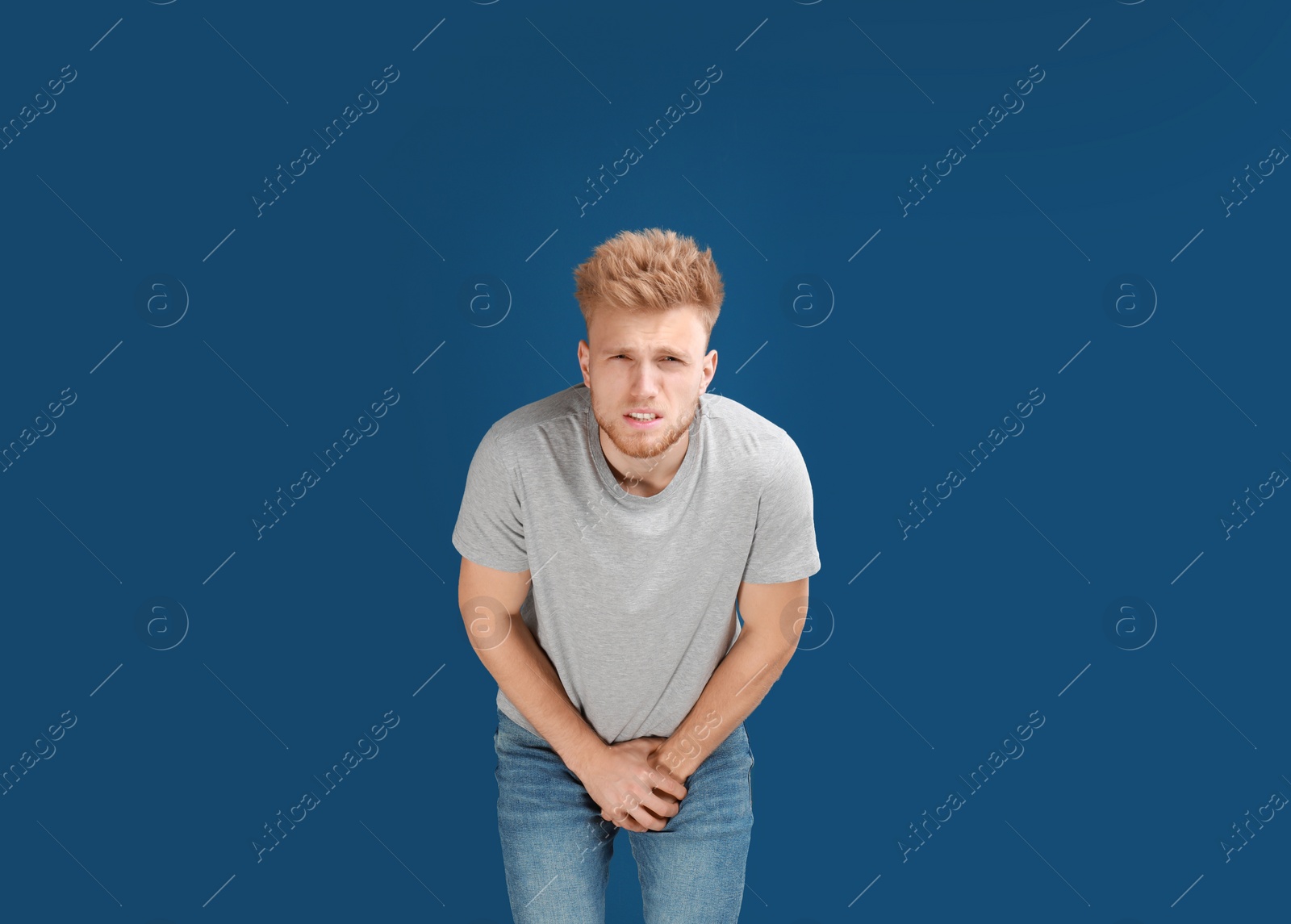 Photo of Young man suffering from pain on blue background. Urology problems