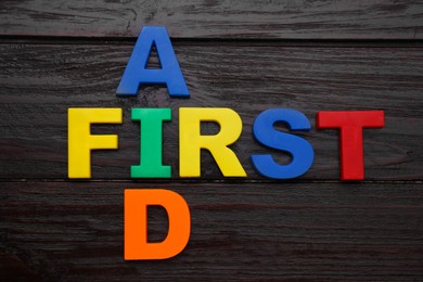 Photo of Words First Aid made of colorful letters on black wooden table, flat lay