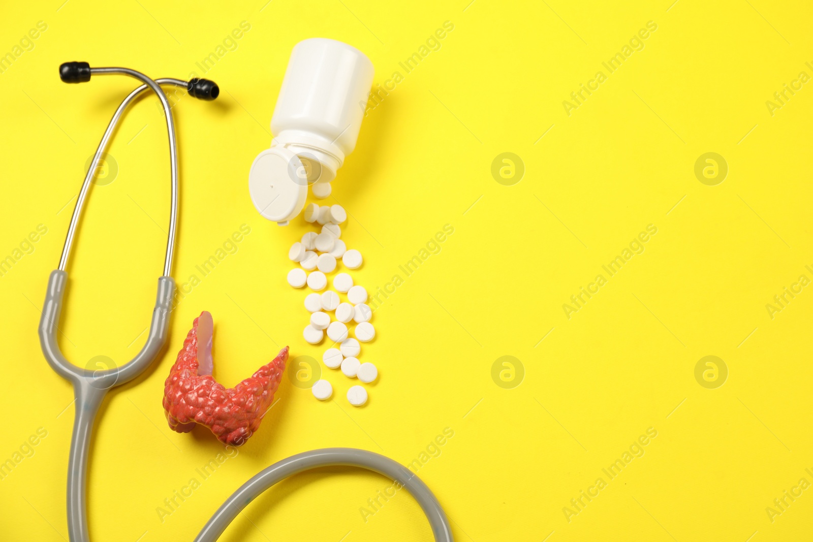 Photo of Endocrinology. Stethoscope, bottle with pills and model of thyroid gland on yellow background, flat lay. Space for text