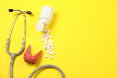 Photo of Endocrinology. Stethoscope, bottle with pills and model of thyroid gland on yellow background, flat lay. Space for text