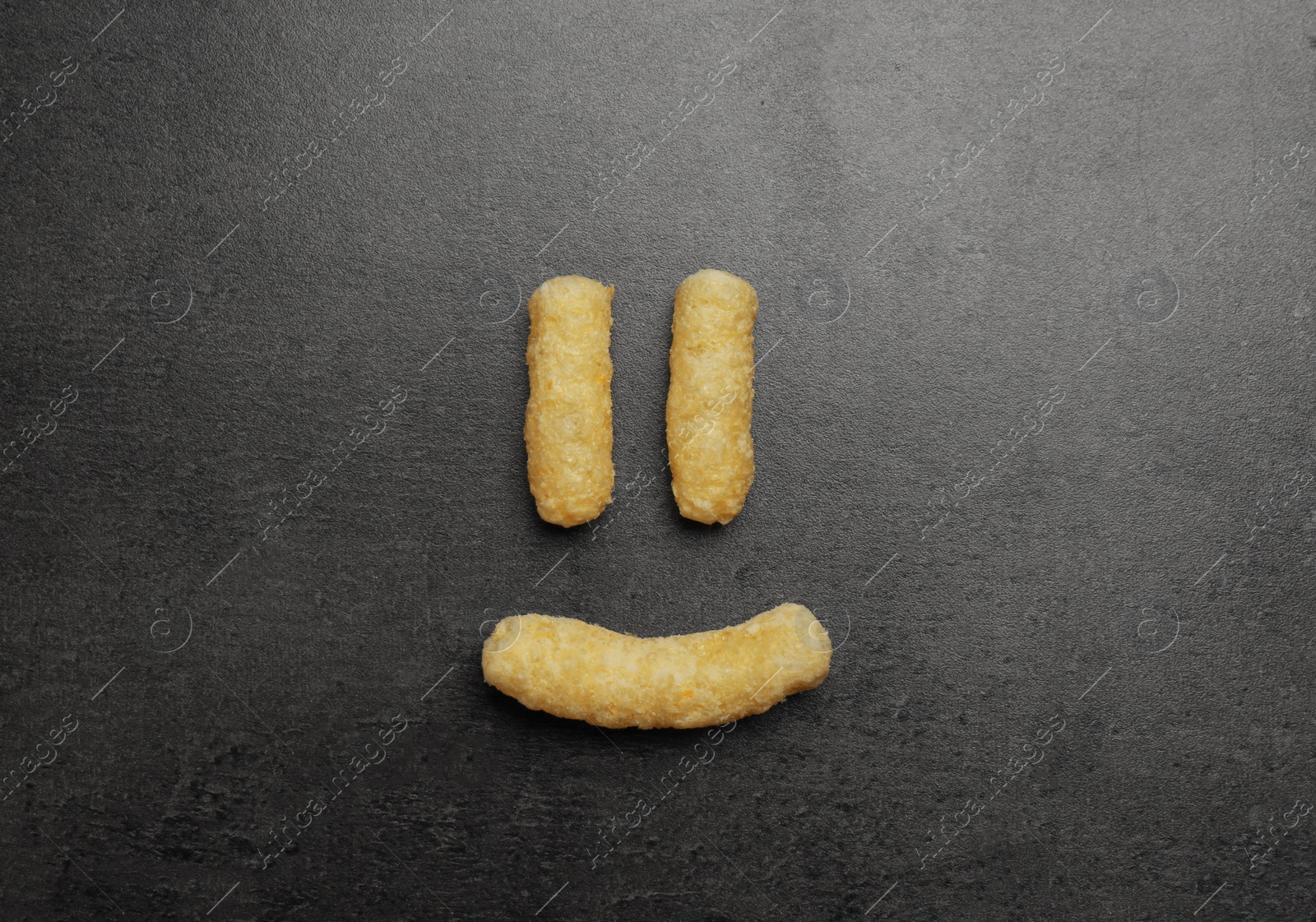 Photo of Funny face made of corn sticks on dark grey table, flat lay