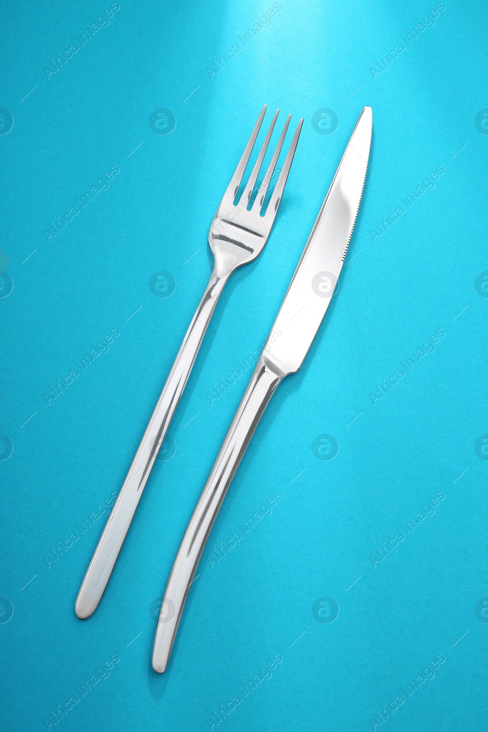 Photo of Shiny fork and knife on light blue background, flat lay