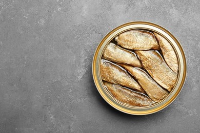 Photo of Sprats in tin can on grey textured table, top view. Space for text