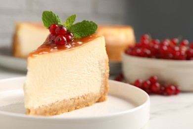 Piece of delicious caramel cheesecake with red currants and mint served on white table, closeup