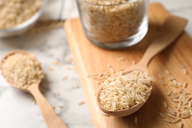 Photo of Uncooked brown rice in wooden spoon on table. Space for text