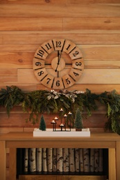 Photo of Christmas decor on console table near wooden wall with clock and garland. Interior design