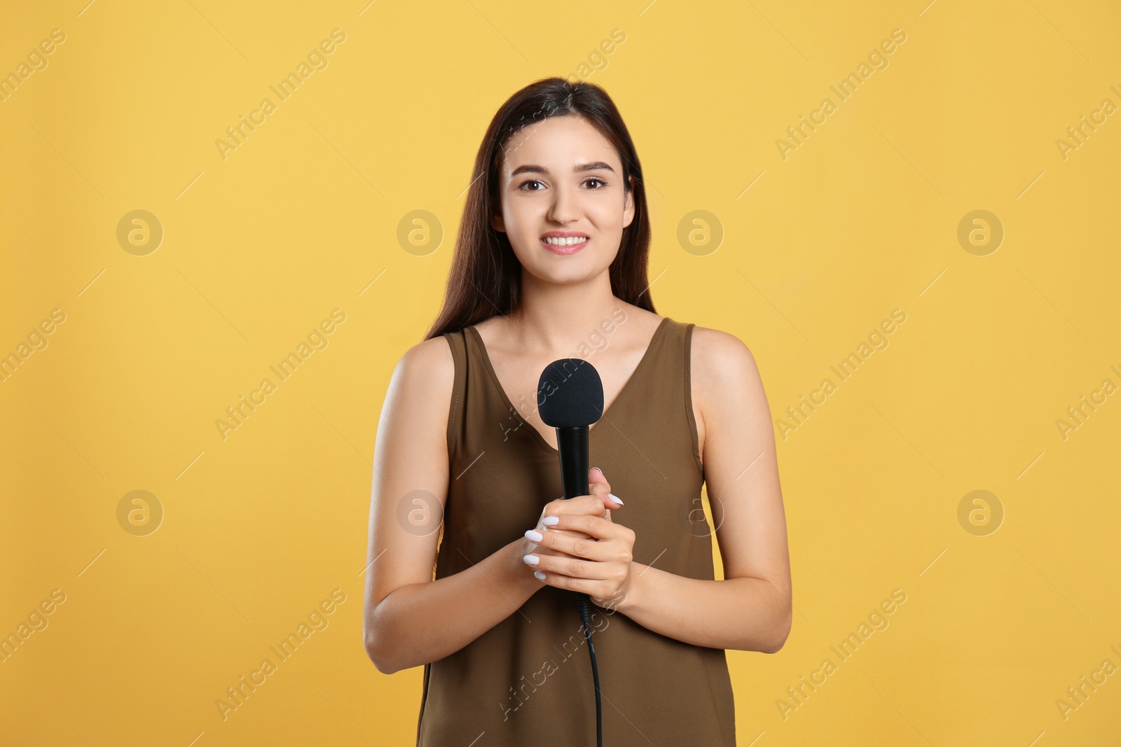 Photo of Young female journalist with microphone on yellow background