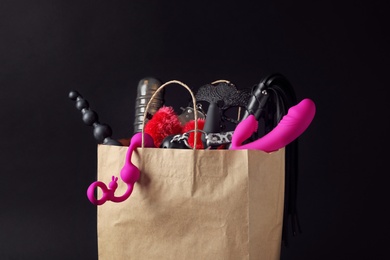 Photo of Paper shopping bag with different sex toys on black background