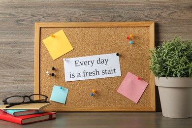 Photo of Cork board with motivational quote Every Day is a Fresh Start, stationery and plant on wooden table