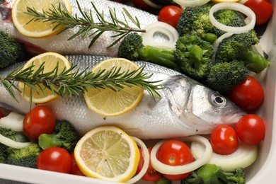 Photo of Raw fish with vegetables and lemon in baking dish, closeup
