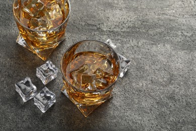 Photo of Whiskey and ice cubes in glasses on grey textured table, space for text