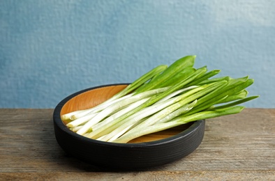 Photo of Plate with wild garlic or ramson on wooden table against color background. Space for text