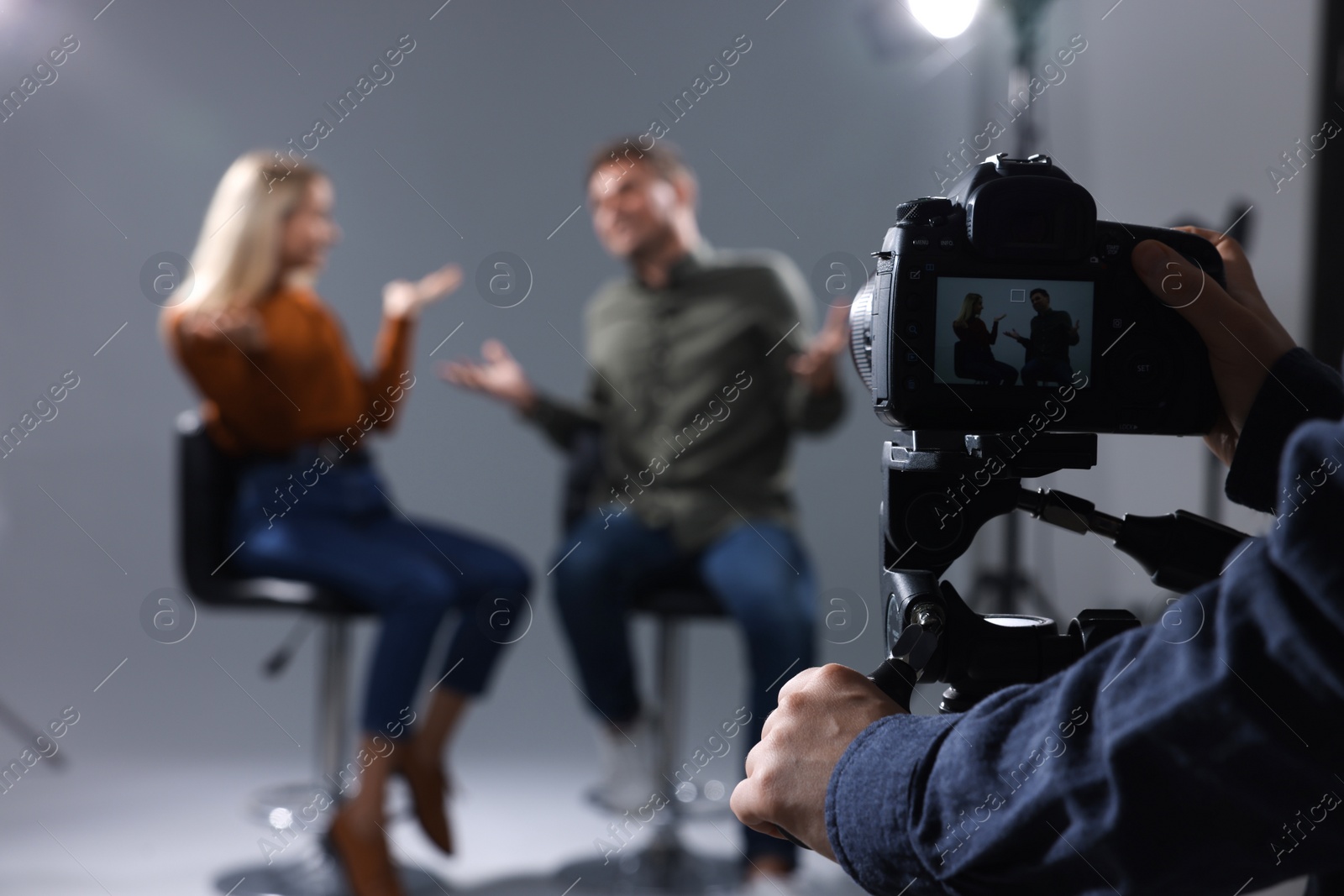 Photo of Casting call. Man and woman performing while camera operator filming them against grey background in studio, selective focus